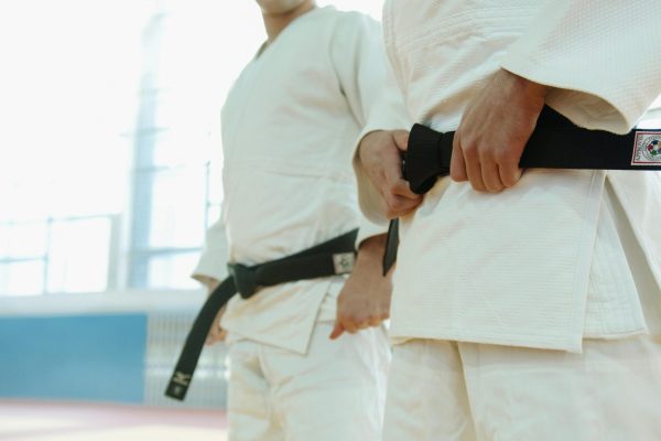 Two martial artists in white uniforms holding black belts, showcasing discipline and strength.