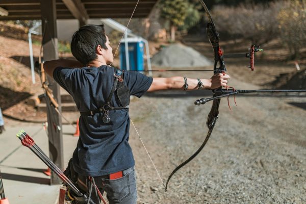 Young man aiming a compound bow at an archery range. Perfect for sports and outdoor lifestyle themes.